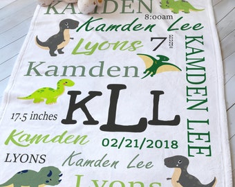 May include: White baby blanket with green dinosaur illustrations and the text "Kamden Lee Lyons" with birth details: 8:00 am, 7 pounds, 17.5 inches, 02/21/2018.