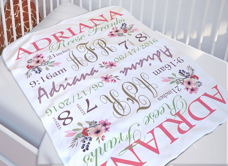 May include: A white baby blanket featuring floral illustrations and personalised text including the name Adriana Reese Franks, the date 17/06/2016, the time 9:16am, the weight 3.4 kg, and the length 53 cm, along with the monogram JFR.