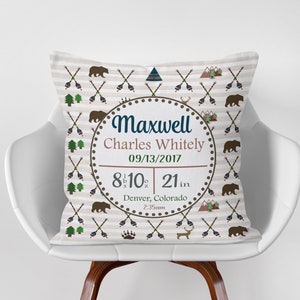 May include: A tan and brown throw pillow with a white background and a repeating pattern of arrows, mountains, and bears. The pillow has a circular design in the center with the text "Maxwell Charles Whitely 09/13/2017 8 lb 10 oz 21 in Denver, Colorado 2:35am".