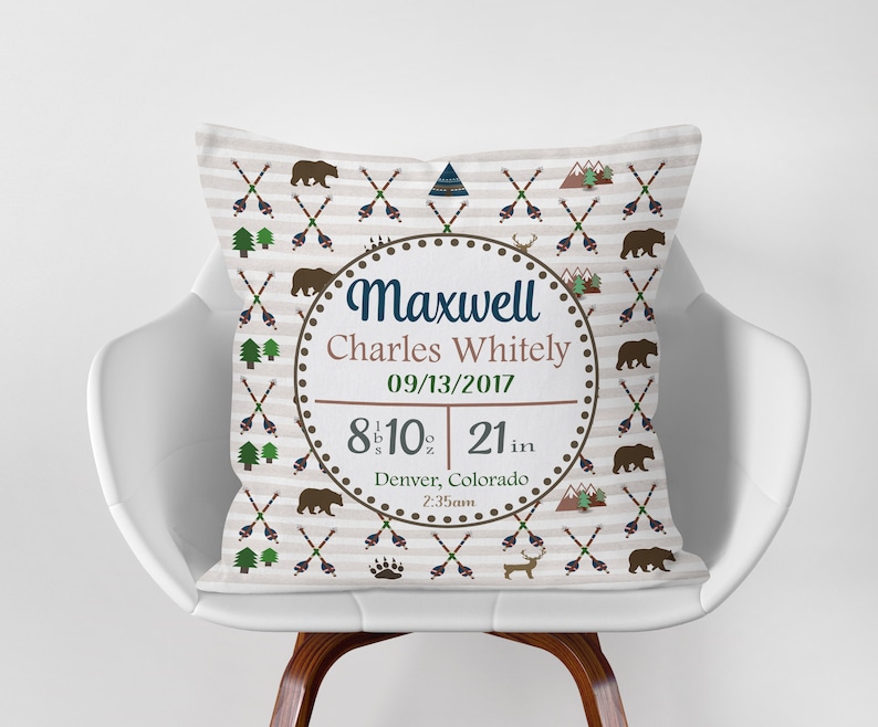 May include: A tan and brown throw pillow with a white background and a repeating pattern of arrows, mountains, and bears. The pillow has a circular design in the center with the text "Maxwell Charles Whitely 09/13/2017 8 lb 10 oz 21 in Denver, Colorado 2:35am".