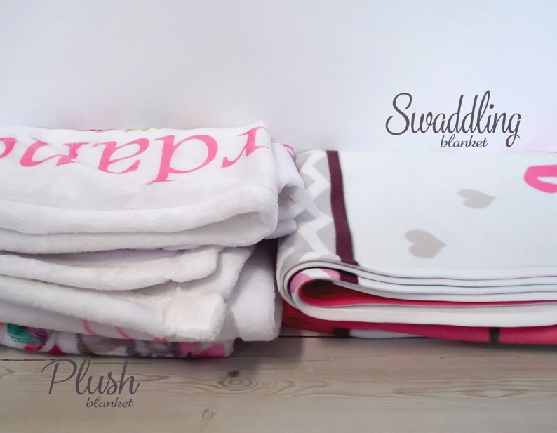 K&ouml;nnte beinhalten: Ein Stapel Babydecken aus Pl&uuml;sch und eine Wickeldecke. Die Pl&uuml;schdecken sind wei&szlig; mit rosa Schrift. Die Wickeldecke ist wei&szlig; mit einem rosa-grauen Zickzackmuster und Herzformen.