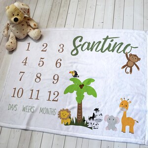 K&ouml;nnte beinhalten: Wei&szlig;e Baby-Meilenstein-Decke mit Dschungel-Thema. Mit dem Namen "Santino" in gr&uuml;ner Schrift, den Zahlen 1-12 und Tierillustrationen wie L&ouml;we, Zebra, Elefant, Giraffe, Tukan und Affe. Enth&auml;lt die W&ouml;rter "Tage, Wochen, Monate".