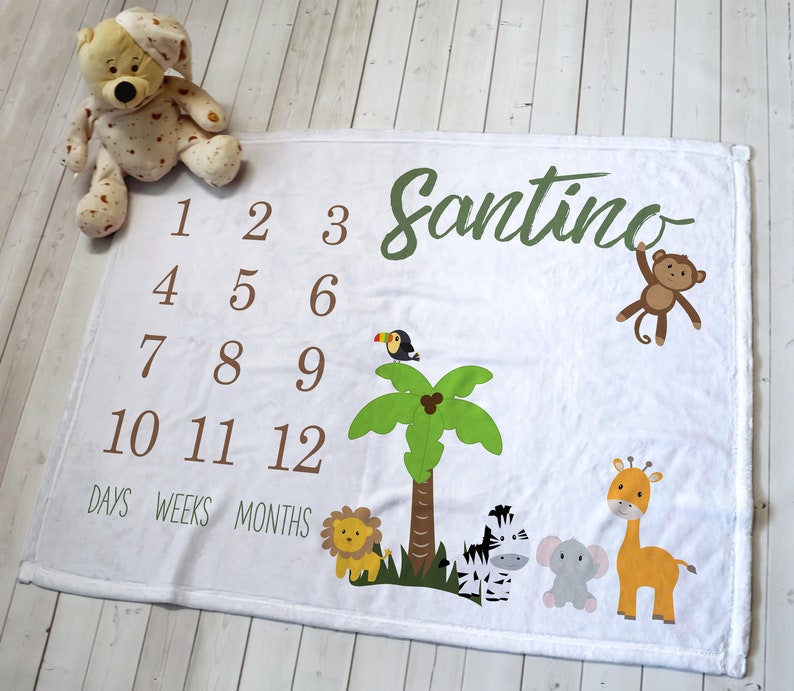 K&ouml;nnte beinhalten: Wei&szlig;e Baby-Meilenstein-Decke mit Dschungel-Thema. Mit dem Namen "Santino" in gr&uuml;ner Schrift, den Zahlen 1-12 und Tierillustrationen wie L&ouml;we, Zebra, Elefant, Giraffe, Tukan und Affe. Enth&auml;lt die W&ouml;rter "Tage, Wochen, Monate".