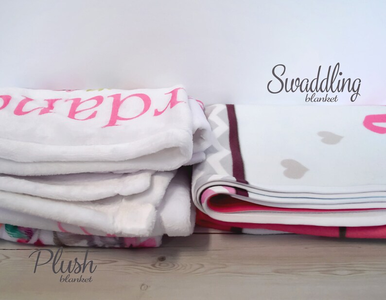 May include: Two folded blankets, one white with pink text "Clara" and one white with gray hearts and a pink border. The white blanket with hearts is labeled "Swaddling blanket" and the white blanket with text is labeled "Plush blanket".