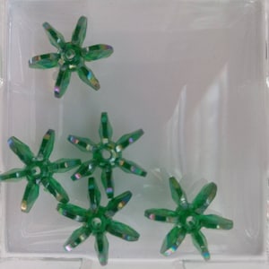 May include: Five green iridescent star-shaped beads with a hole in the center. The beads are on a white surface.