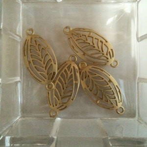 May include: Four gold-colored metal leaf-shaped charms with a cut-out design. The charms have a loop at each end for attaching to jewelry or other crafts.