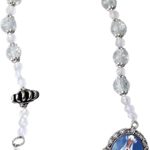 May include: A rosary with clear, faceted beads and smaller white beads. The rosary features a silver-toned cross and a pendant with an image of a religious figure. The beads are connected by a silver-toned chain.