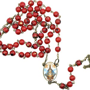 Könnte beinhalten: Ein Rosenkranz mit roten, gesprenkelten Perlen und einer antiken, messingfarbenen Metallkette und -akzenten. Der Rosenkranz enthält ein Kruzifix und ein Mittelstück mit einem religiösen Bild. Die Perlen haben einen Durchmesser von etwa 8 mm.