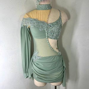 May include: A sage green dance costume with a sheer bodice, one long sleeve, and a gathered skirt. The bodice is embellished with lace and rhinestones.