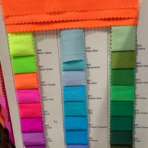 May include: A fabric colour chart displaying a range of shades. The swatches include neon yellow, neon green, neon orange, pinks, blues, greens, and purples. The card also shows the names of the colours, such as Baby Blue, Aquamarine, and Teal.