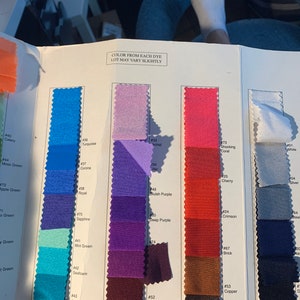 May include: A colour swatch book displaying a range of fabrics in shades of blue, purple, pink, red, and brown. The text "COLOR FROM EACH DYE LOT MAY VARY SLIGHTLY" is printed at the top. Each colour is labelled with a number and a name.