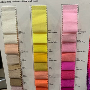 May include: Swatch card displaying a range of sheer stretch mesh fabric colours. The fabric comes in widths of 58" or 60". The colours include off white, ivory, light peach, natural, mocha, khaki, sable, dark rose, lemon yellow, samba yellow, yellow, athletic gold, gold, cantaloupe, orange, paprika, bubblegum pink, blush pink, medium pink, sweet potato, deep pink, lipstick, fuchsia, and raspberry.