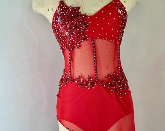 May include: A red dance costume with a halter neckline and a sheer midriff. The bodice is heavily embellished with sequins and beads. The costume includes a matching neck piece. The skirt has an asymmetrical hemline.