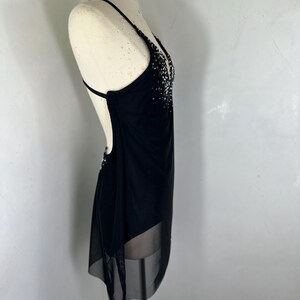 Puede incluir: Un vestido negro sin mangas con una superposici&oacute;n transparente y un escote de cuentas. El vestido est&aacute; en un maniqu&iacute; blanco.