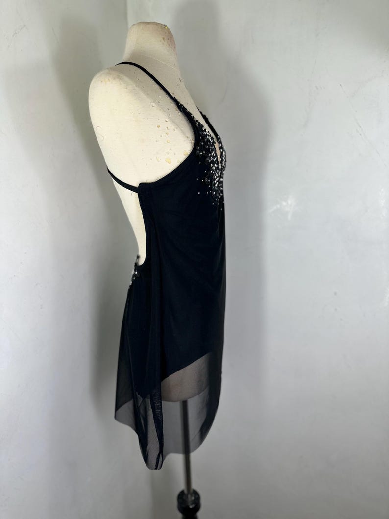 Puede incluir: Un vestido negro sin mangas con una superposici&oacute;n transparente y un escote de cuentas. El vestido est&aacute; en un maniqu&iacute; blanco.
