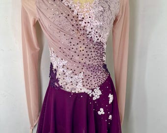 May include: A long-sleeved figure skating dress with a pink and purple ombre bodice and a purple skirt. The bodice is adorned with white lace and rhinestones. The skirt is made of a flowing fabric.