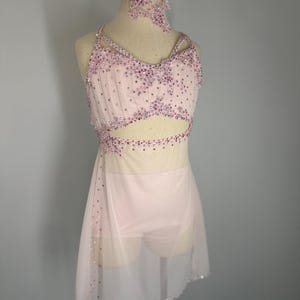 May include: A pale pink dance costume with a halter top and a skirt. The bodice is decorated with sparkling crystals and a cut-out design. The skirt is sheer and falls to the knees. A matching neck piece is also included.