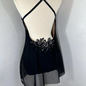 Puede incluir: Vestido de baile negro con una superposici&oacute;n transparente y un dise&ntilde;o de cuentas en la espalda.
