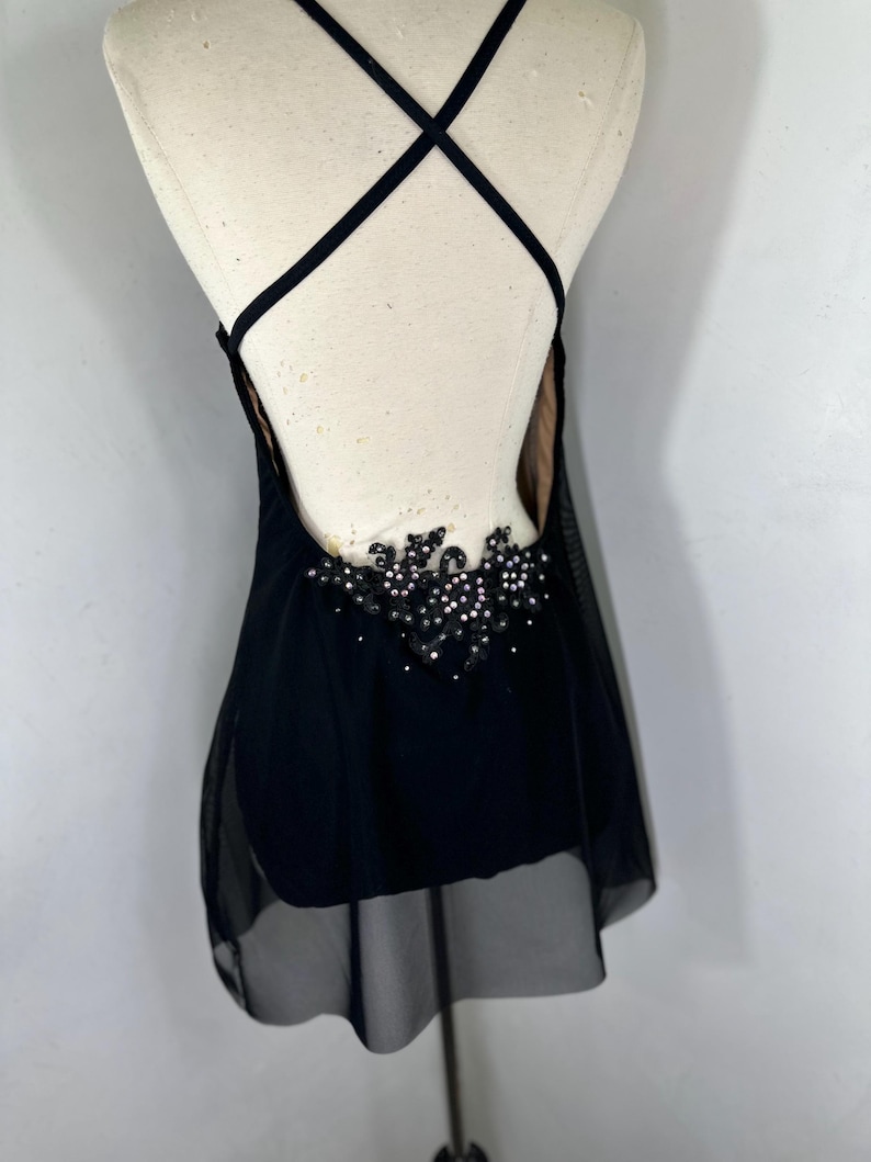 Puede incluir: Vestido de baile negro con una superposici&oacute;n transparente y un dise&ntilde;o de cuentas en la espalda.