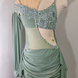May include: A sage green dance costume with a sheer bodice and long sleeve. The bodice is embellished with silver sequins and beads, and the skirt is gathered and ruffled.