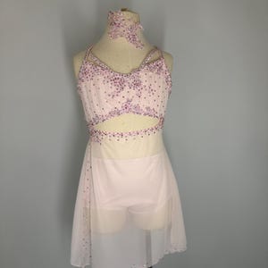 May include: A pale pink dance costume with a matching choker. The bodice is decorated with pink rhinestones and has a cut-out design. The skirt is a sheer, flowing fabric, also embellished with rhinestones.