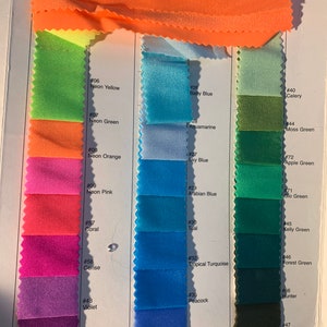 May include: A fabric colour swatch card displaying a range of vibrant colours. The card shows swatches of neon yellow, green, pink, orange, coral, cerise, violet, and hibiscus. Additional colours include baby blue, aquamarine, sky blue, teal, and tropical turquoise.