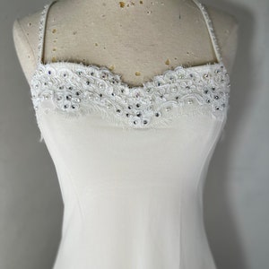 May include: A white sleeveless dress with a lace and rhinestone trim around the neckline.