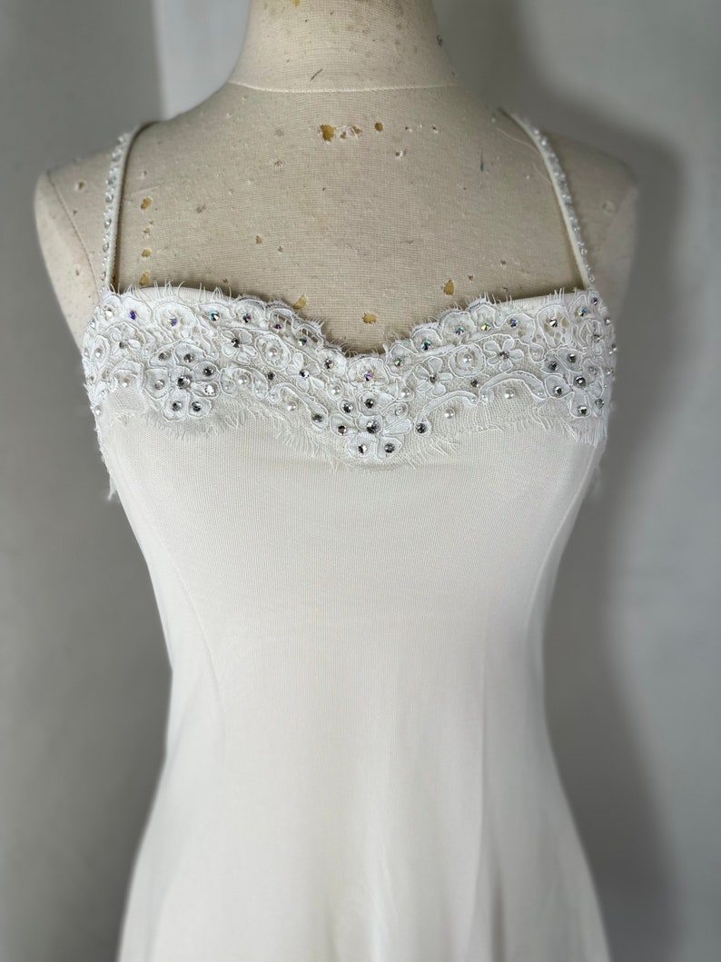 May include: A white sleeveless dress with a lace and rhinestone trim around the neckline.