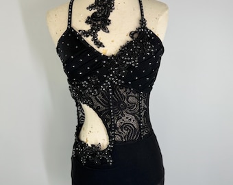 May include: A black dance leotard with detailed beading and lace. It has a halter neck, cut-out design, and a sheer skirt. The bodice is adorned with sparkling embellishments, creating a glamorous appearance.