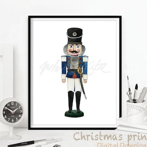 Puede incluir: Una pintura de acuarela de un cascanueces tradicional. El cascanueces lleva un uniforme azul y blanco con una faja roja y un sombrero negro. Sostiene una espada en su mano derecha y tiene bigote y barba.
