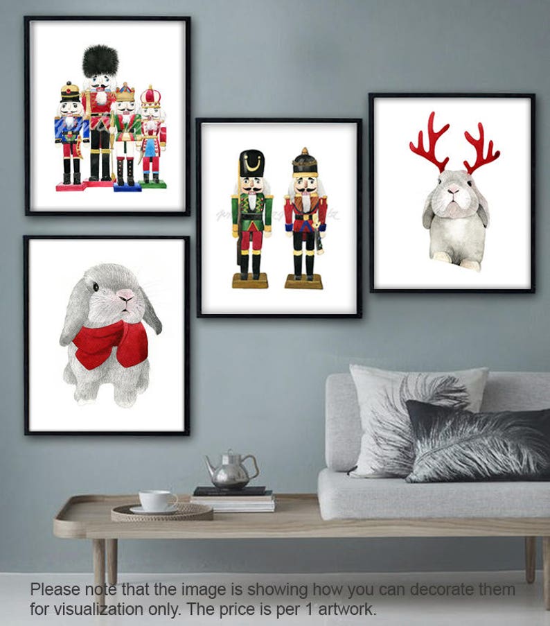 May include: A set of four framed prints featuring watercolor illustrations of nutcracker soldiers and bunnies wearing antlers and a red scarf. The prints are displayed on a wall above a couch with pillows.