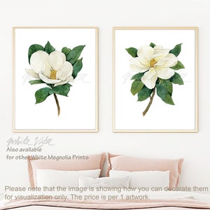 May include: Two framed watercolor prints of white magnolia flowers with green leaves on a white background. The prints are hanging on a white wall above a pink bed.