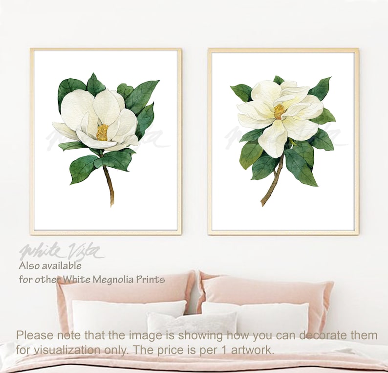 May include: Two framed watercolor prints of white magnolia flowers with green leaves on a white background. The prints are hanging on a white wall above a pink bed.