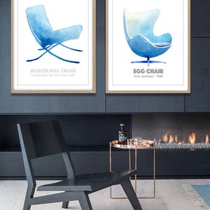 May include: Two watercolor prints of iconic chairs, the Barcelona Chair by Ludwig Mies Van Der Rohe and the Egg Chair by Arne Jacobsen. The prints are framed in wood and displayed on a wall above a fireplace.