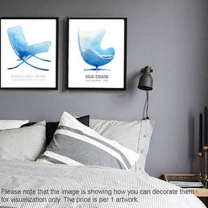 May include: Two watercolor illustrations of iconic chairs: a blue Barcelona chair and a blue Egg chair. The illustrations are framed and displayed on a gray wall above a striped bed.
