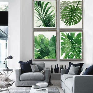K&ouml;nnte beinhalten: Vier gerahmte Aquarellbilder von tropischen Bl&auml;ttern in Gr&uuml;nt&ouml;nen. Die Bilder sind in einem Raster auf einer wei&szlig;en Wand &uuml;ber einem grauen Sofa angeordnet.