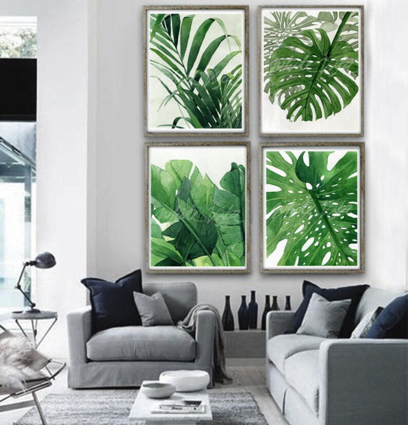 K&ouml;nnte beinhalten: Vier gerahmte Aquarellbilder von tropischen Bl&auml;ttern in Gr&uuml;nt&ouml;nen. Die Bilder sind in einem Raster auf einer wei&szlig;en Wand &uuml;ber einem grauen Sofa angeordnet.
