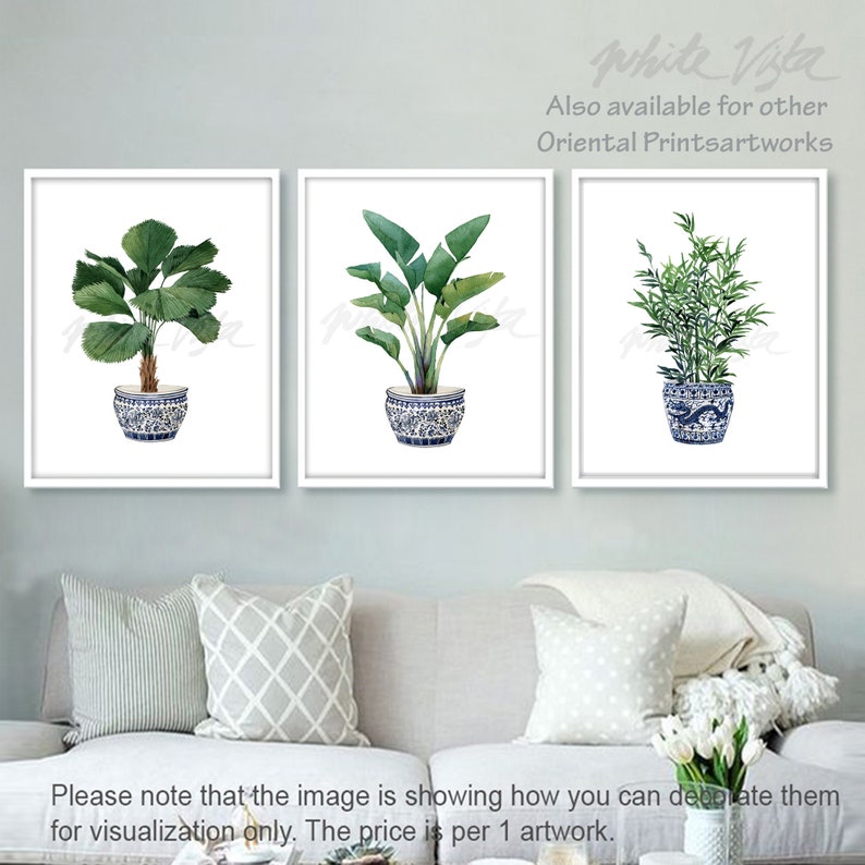 May include: Three watercolor paintings of plants in blue and white ceramic pots. The plants are a palm tree, a banana leaf plant, and bamboo. The paintings are framed in white.