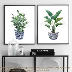 May include: Two watercolor prints of plants in blue and white ceramic pots. The print on the left features a green leafy plant, while the print on the right features a green tropical plant with large leaves.