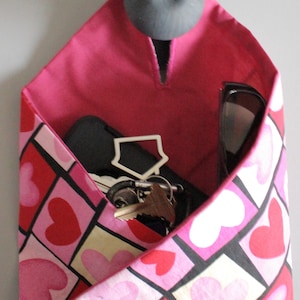 May include: A pink fabric wall organizer with a heart pattern, holding keys, a phone, and a house-shaped keychain. The organizer is mounted on a wall with a gray knob. The interior is a solid pink color.