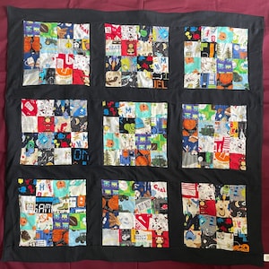 May include: A black and white quilt with a patchwork design. The quilt is made up of squares of different fabrics, each with a different pattern. The patterns include cars, animals, and other designs. The quilt is bordered in black fabric.