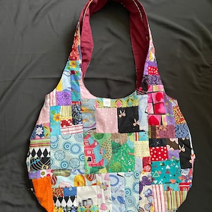 May include: A patchwork tote bag with a variety of colorful fabrics and patterns. The bag has a long strap and is made of a soft, durable material.