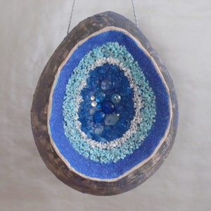 May include: A blue and white geode-shaped ornament with a brown outer shell. The geode is filled with blue and white glitter and small blue glass beads.