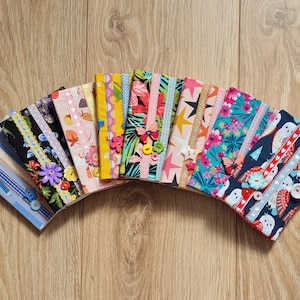 May include: A collection of 13 colorful fabric pouches with various patterns and designs, including floral, geometric, and animal prints. Each pouch has a button closure and a ribbon detail.