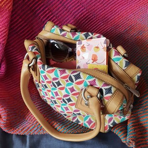 Pode incluir: Uma bolsa de m&atilde;o de couro marrom com um padr&atilde;o geom&eacute;trico colorido. A bolsa tem um fecho de correr e uma al&ccedil;a superior. Uma carteira de tecido com padr&atilde;o rosa e branco est&aacute; dentro da bolsa.