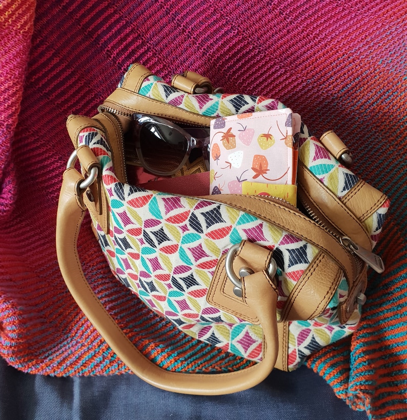 Pode incluir: Uma bolsa de m&atilde;o de couro marrom com um padr&atilde;o geom&eacute;trico colorido. A bolsa tem um fecho de correr e uma al&ccedil;a superior. Uma carteira de tecido com padr&atilde;o rosa e branco est&aacute; dentro da bolsa.