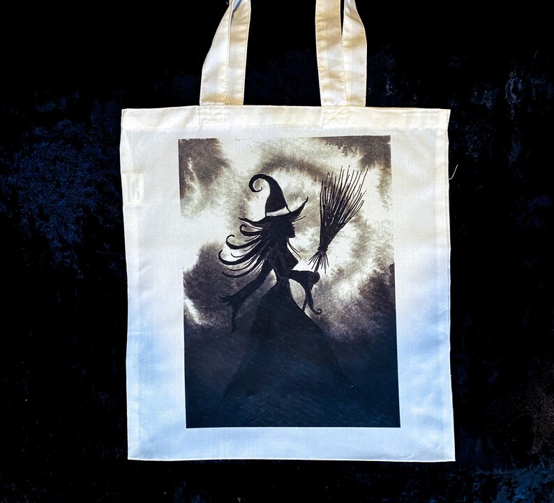 Pu&ograve; includere: Borsa tote bianca con un'illustrazione in bianco e nero di una strega con una scopa in un cielo nuvoloso.