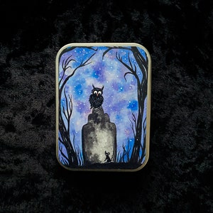 May include: A black and white illustration of an owl perched on a rock in a woodland setting. The background is a watercolour wash of blue and purple with white stars. A small mouse is standing in the foreground.