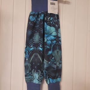 Puede incluir: Pantalones azules con fondo azul marino oscuro y un estampado floral y abstracto en tonos turquesa y azul claro. La prenda cuenta con una cintura el&aacute;stica ancha de color azul s&oacute;lido y pu&ntilde;os el&aacute;sticos a juego en los tobillos. Etiqueta blanca.