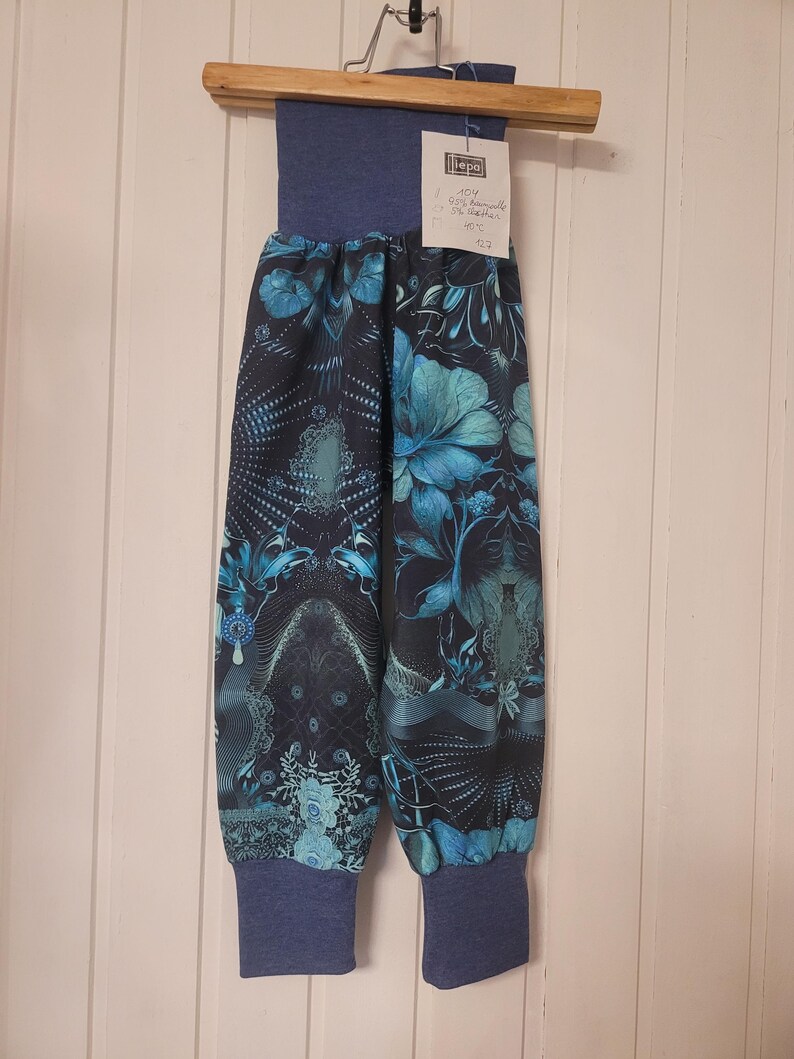 Puede incluir: Pantalones azules con fondo azul marino oscuro y un estampado floral y abstracto en tonos turquesa y azul claro. La prenda cuenta con una cintura el&aacute;stica ancha de color azul s&oacute;lido y pu&ntilde;os el&aacute;sticos a juego en los tobillos. Etiqueta blanca.